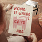 Katzenprint „Home is where the cats are“ in Händen, rosa Katze, rote Schrift, ungerahmt