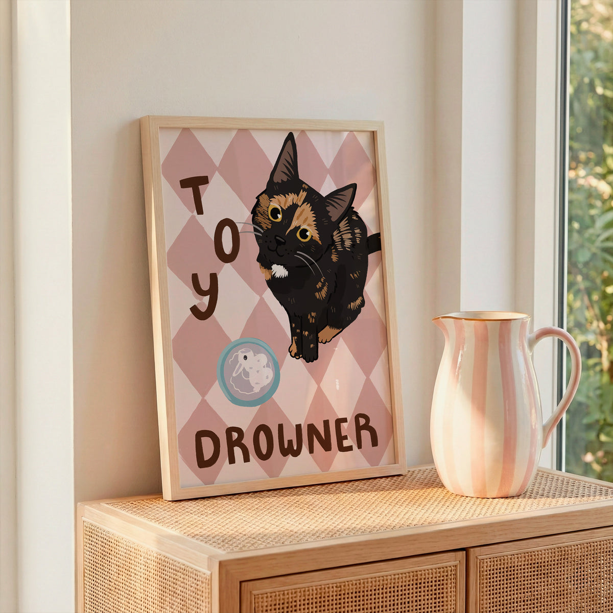 Cat print artwork on light wood surface, black kitten over tan-pink diamond pattern