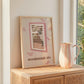 Framed cat spy print on stand with window bars and 'NEIGHBOURHOOD SPY' text, pink accents.
