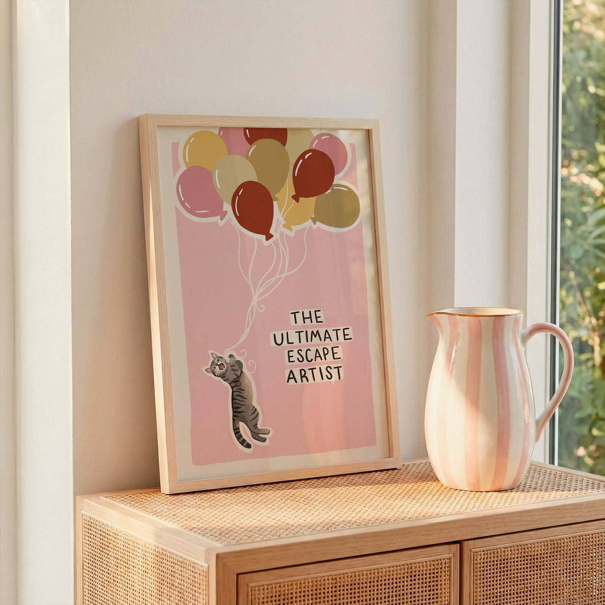 Cat print artwork with balloon cluster and gray tabby cat illustration, shown on a tabletop.
